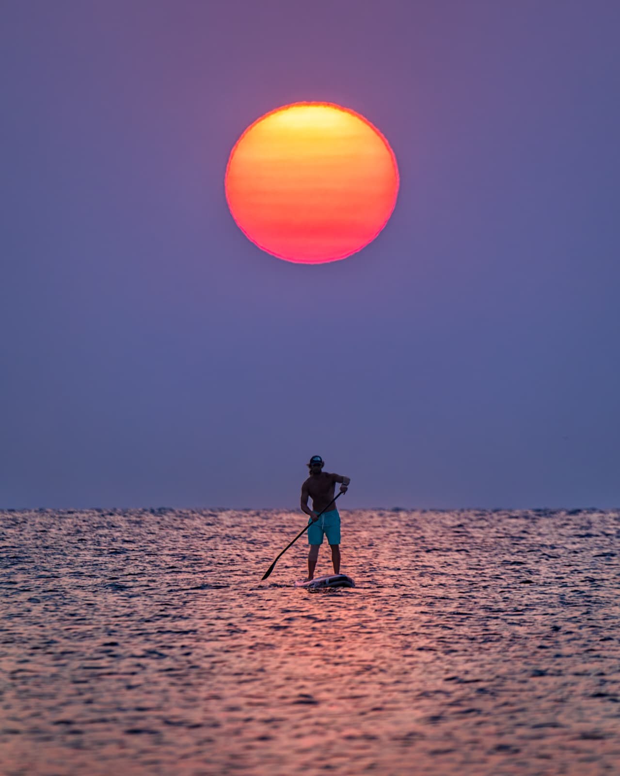 Persona remando en paddle surf bajo el sol al atardecer