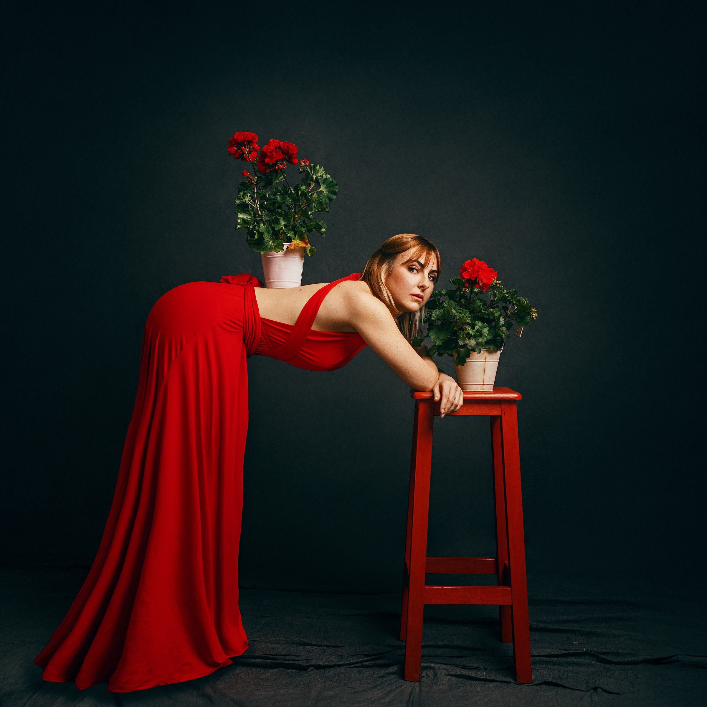 Fotografía de Mara Saiz: figura con vestido rojo entre plantas y fondo oscuro