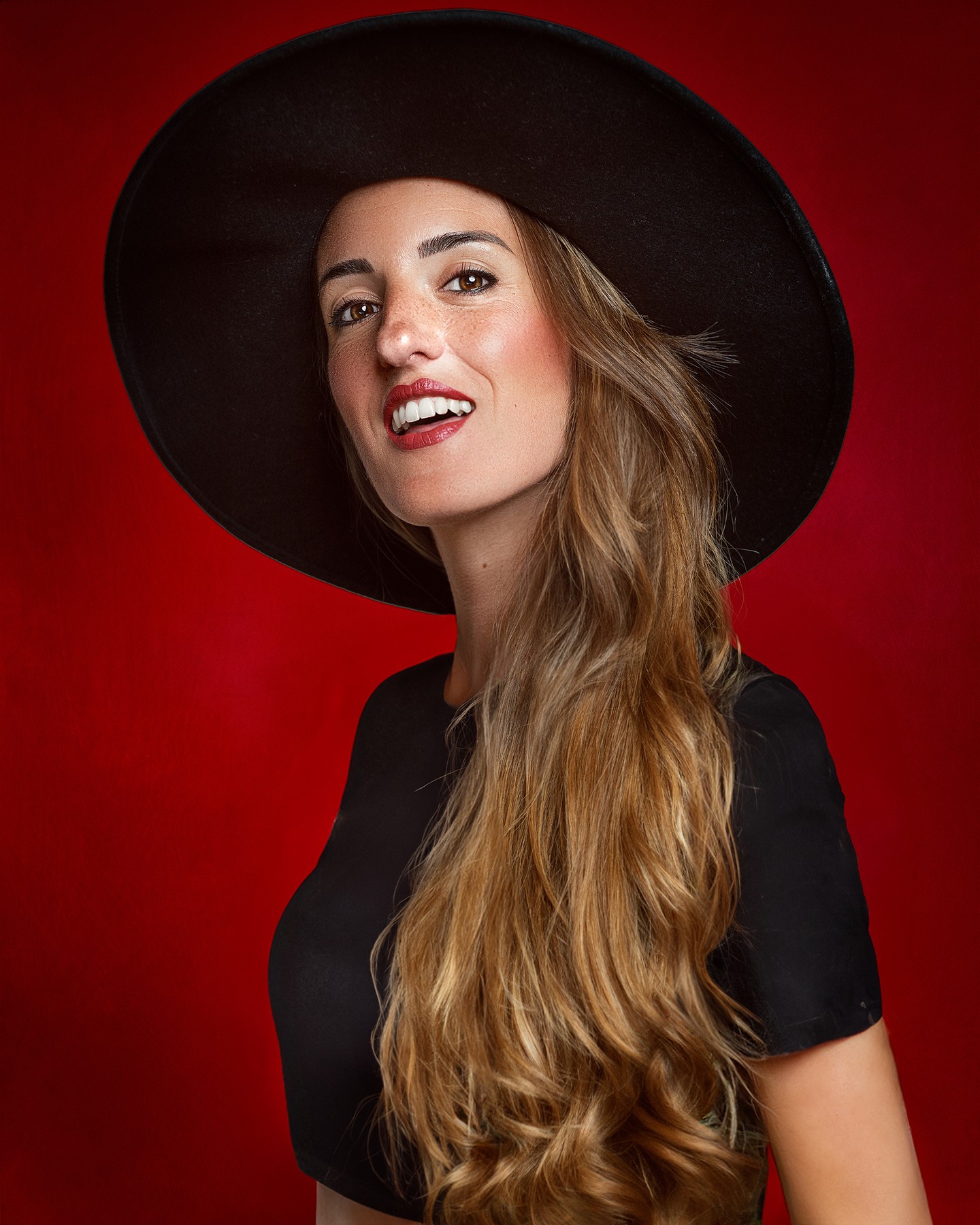 Mara Saiz sonríe con sombrero negro sobre fondo rojo