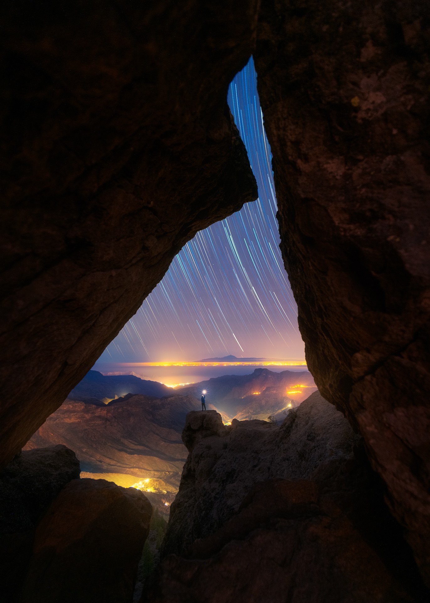 Paisaje nocturno enmarcado por una cueva con una figura bajo las estrellas, fotografía de David Rodríguez